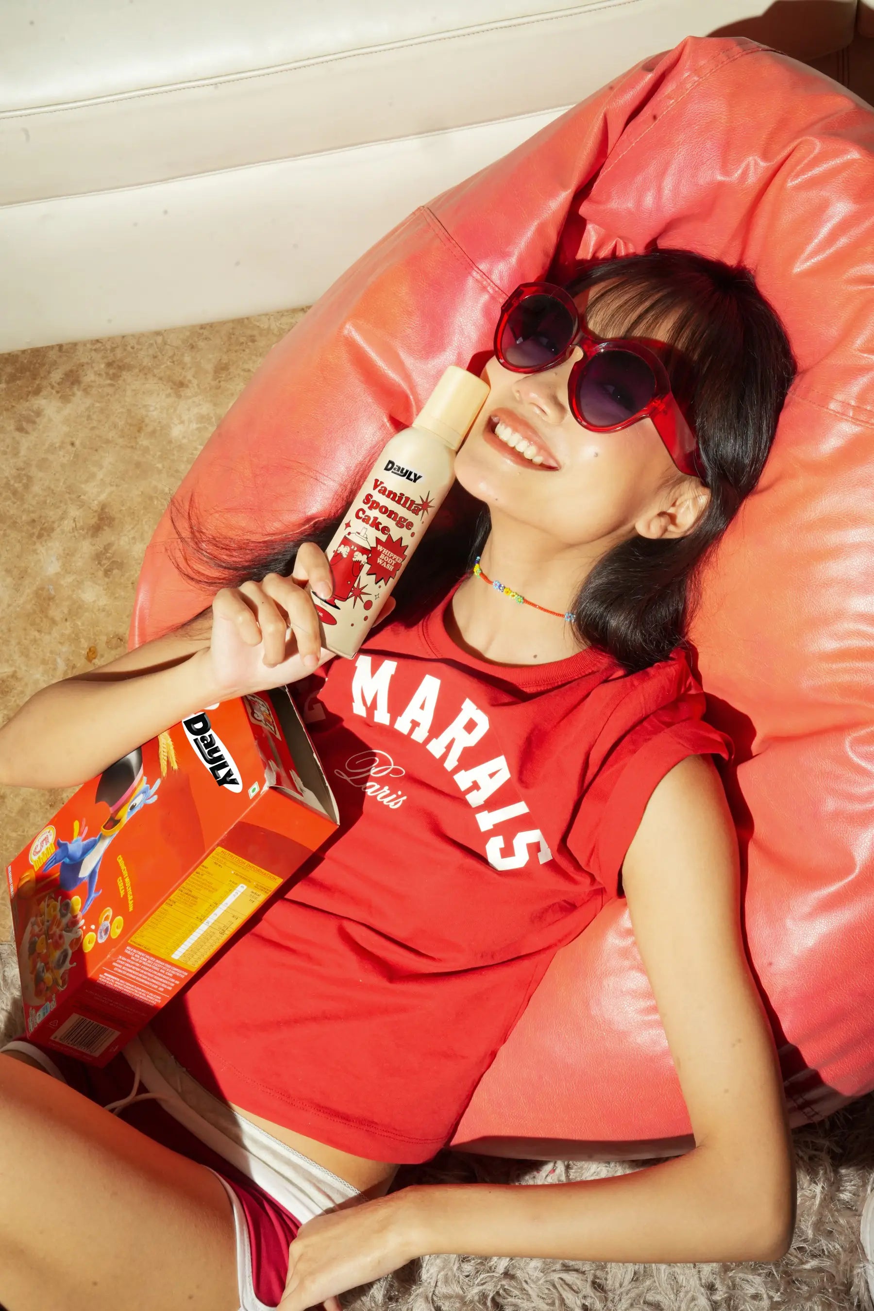 Model relaxing on a pink beanbag, holding Vanilla Sponge Cake whipped body wash